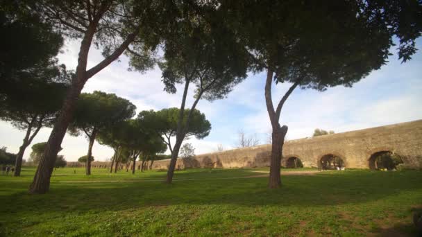 Ön planda ağaçlar ve arka planda su kemerleri olan Parco degli Acquedotti 'nin etrafında yürüyen insanların görüntüsü. — Stok video