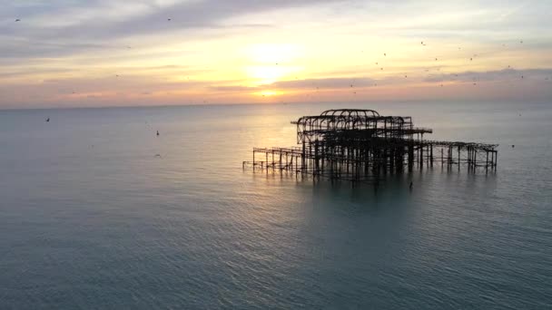 夕暮れ時にイギリスのブライトンで火災で焼失した桟橋の遺跡を周回する空中ショット — ストック動画