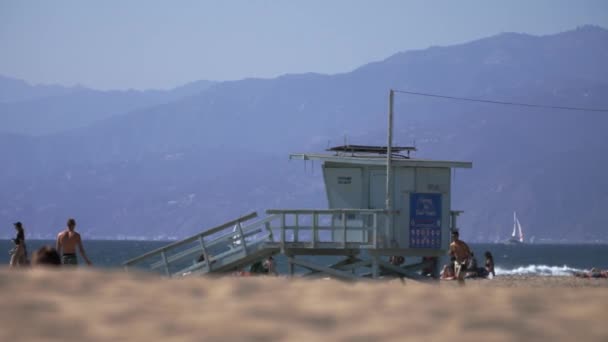 Des hommes lancent une balle devant une cabane de sauveteurs, à Venice Beach, Los Angeles — Video