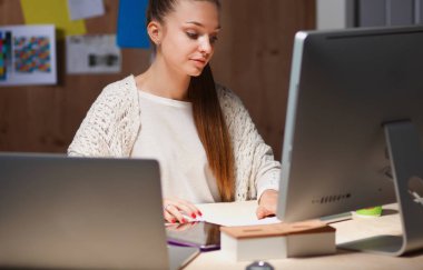 Ofiste çalışan genç bir kadın, masada oturuyor.