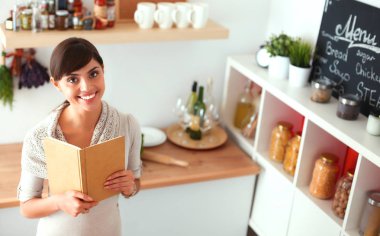 Mutfakta yemek kitabı okuyan genç bir kadın yemek tarifi arıyor.