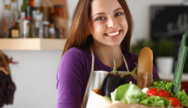 Jonge vrouw met boodschappentas met groenten Staande in de keuken — Stockfoto