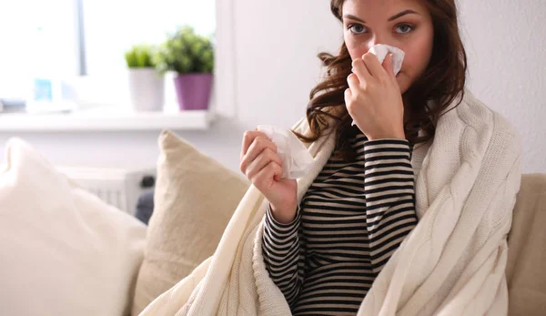 Portrait of a sick woman blowing her nose while sitting on the sofa — Stock Photo, Image