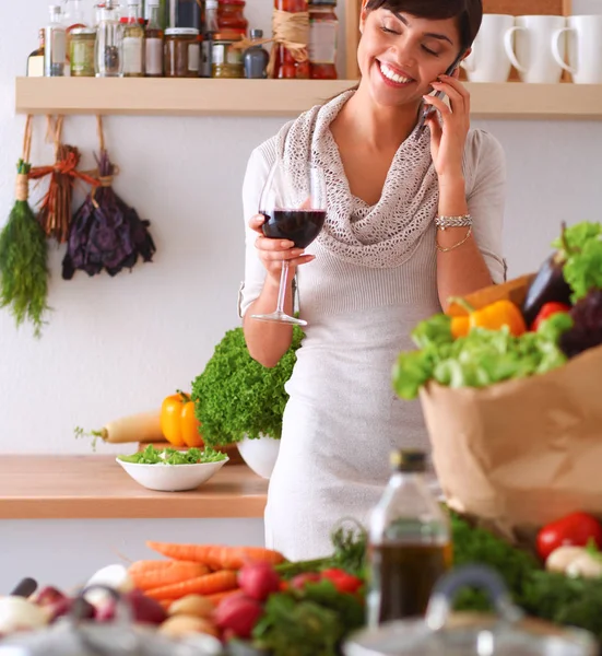 Young woman cutting vegetables in kitchen, holding a glass of wine — Stock Photo, Image