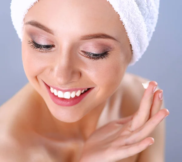 Hermosa joven aplicando una crema en su cara aislada sobre fondo gris — Foto de Stock