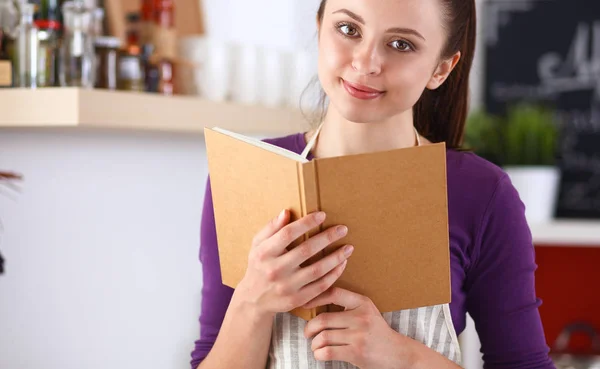 Jonge vrouw die kookboek leest in de keuken, op zoek naar recept — Stockfoto