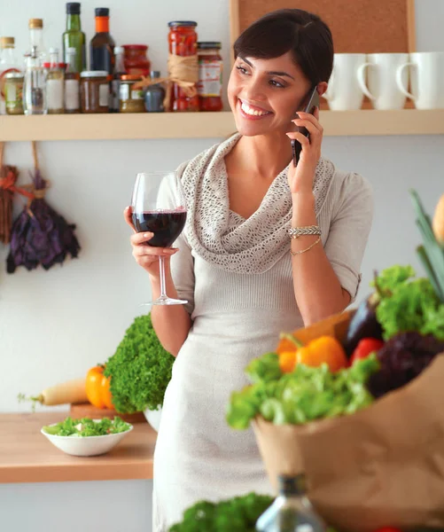 Mujer joven cortando verduras en la cocina, sosteniendo una copa de vino —  Fotos de Stock