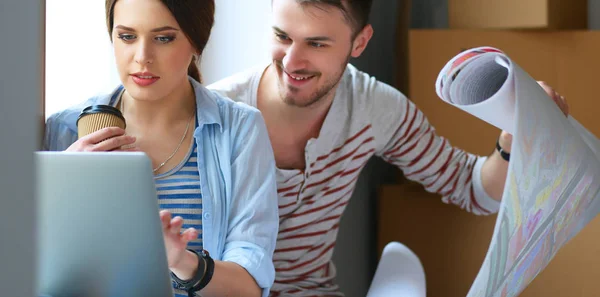 Young couple sitting on the floor and looking at the blueprint of new home — Stock Photo, Image