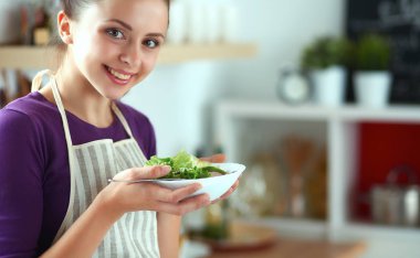 Genç kadın modern mutfakta taze salata yiyor.