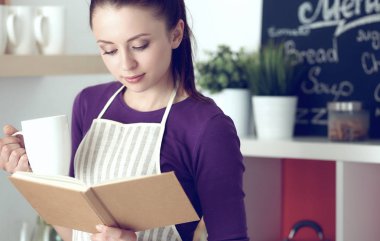 Mutfakta yemek kitabı okuyan genç bir kadın yemek tarifi arıyor.