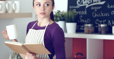 Mutfakta yemek kitabı okuyan genç bir kadın yemek tarifi arıyor.
