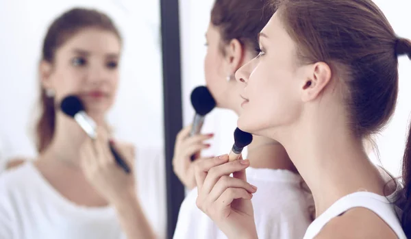 Beautiful girls looking in the mirror and applying cosmetic with a big brush — Stock Photo, Image