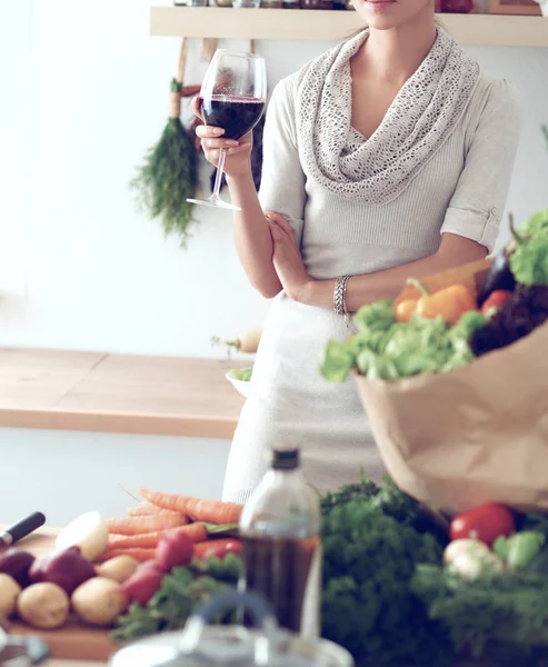 Jeune femme coupant des légumes dans la cuisine, tenant un verre de vin — Photo