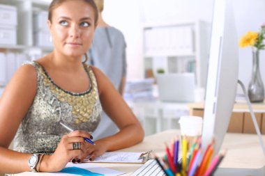 Moda tasarımcıları stüdyoda çalışıyor. Masanın üzerinde oturuyorlar.