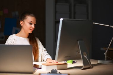 Ofiste çalışan genç bir kadın, masada oturuyor.