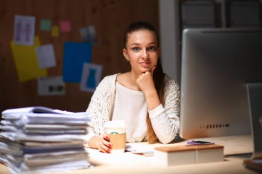 Ofiste çalışan genç bir kadın, masada oturuyor.