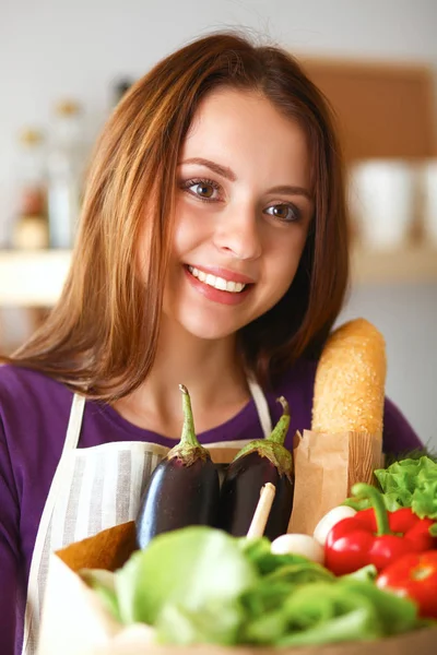Νεαρή γυναίκα κρατά τσάντα ψώνια με λαχανικά Στέκεται στην κουζίνα — Φωτογραφία Αρχείου