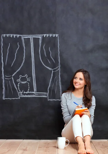 Junge Frau sitzt auf dem Boden in der Nähe einer dunklen Wand mit gemaltem Fenster — Stockfoto