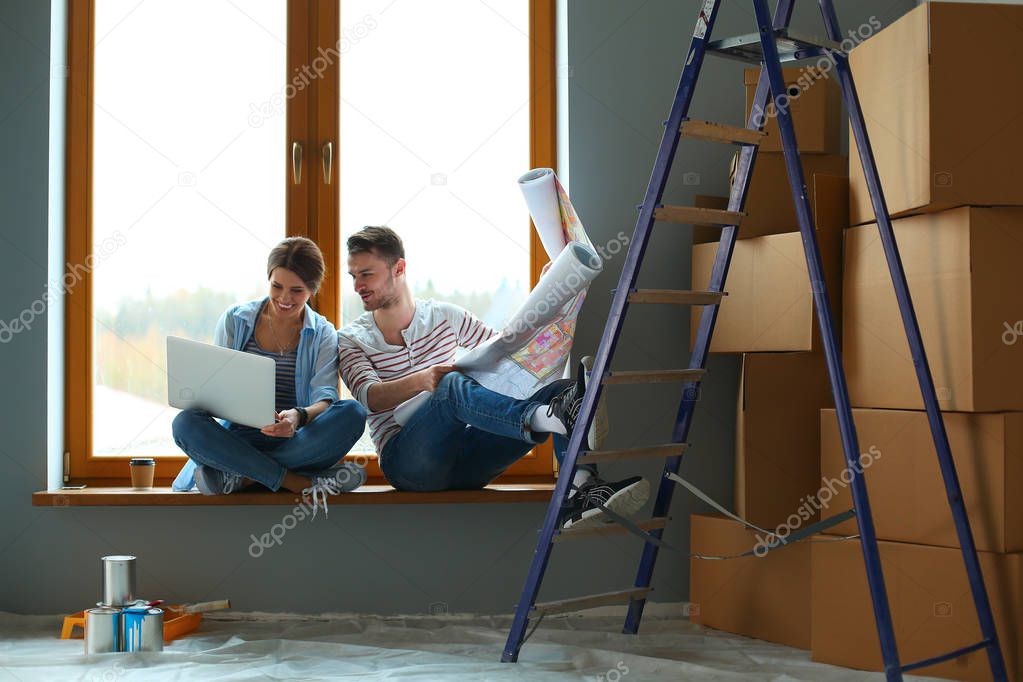 Young couple sitting on the floor and looking at the blueprint of new home