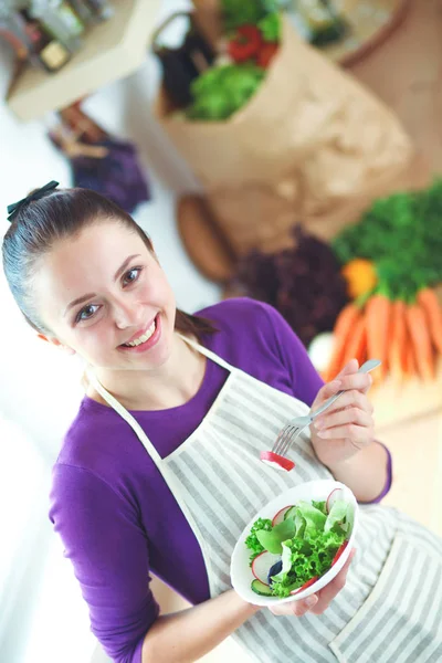 Mujer joven comiendo ensalada fresca en la cocina moderna — Foto de Stock