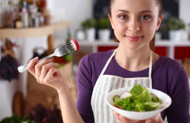 Genç kadın modern mutfakta taze salata yiyor.