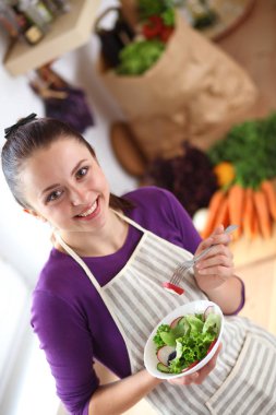 Genç kadın modern mutfakta taze salata yiyor.