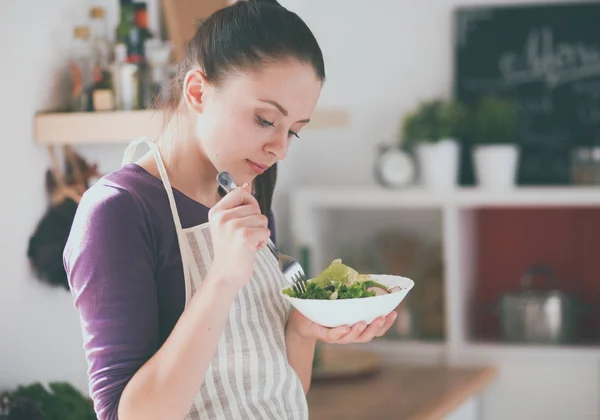 Mujer joven comiendo ensalada fresca en la cocina moderna — Foto de Stock