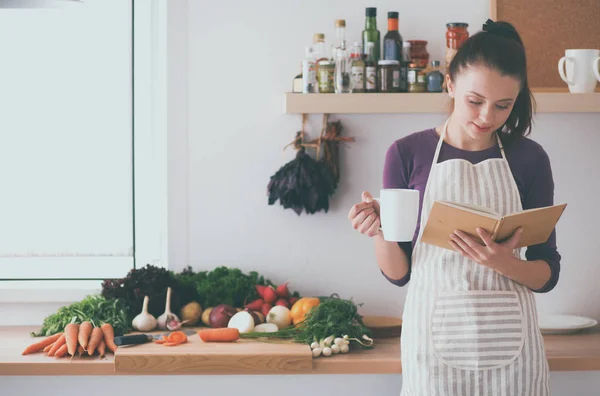 Jonge vrouw die kookboek leest in de keuken, op zoek naar recept — Stockfoto