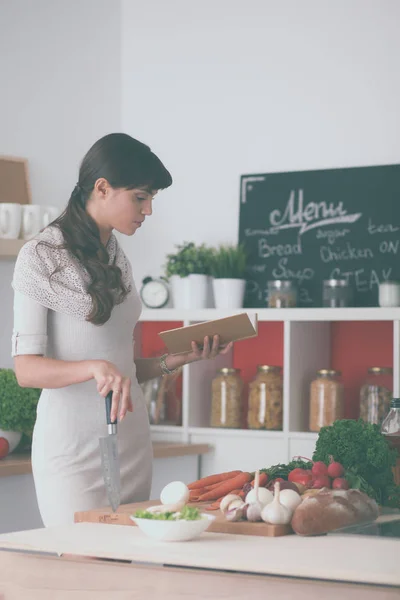 Jovem mulher lendo livro de receitas na cozinha, à procura de receita — Fotografia de Stock