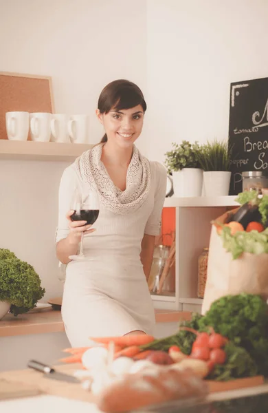 Jeune femme coupant des légumes dans la cuisine, tenant un verre de vin — Photo