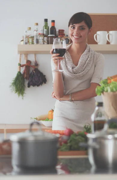 Молодая женщина режет овощи на кухне, держа бокал вина — стоковое фото