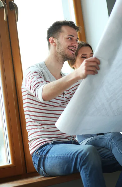 Giovane coppia seduta sul pavimento e guardando il progetto della nuova casa — Foto Stock