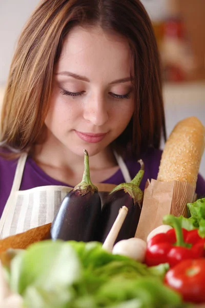 Mujer joven sosteniendo bolsa de la compra de comestibles con verduras de pie en la cocina — Foto de Stock