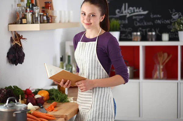 Jovem mulher lendo livro de receitas na cozinha, à procura de receita — Fotografia de Stock