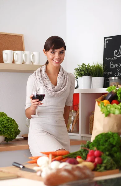 Junge Frau schneidet Gemüse in Küche und hält ein Glas Wein in der Hand — Stockfoto