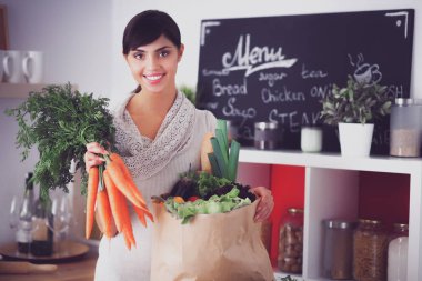 Mutfakta havuç tutan genç ve mutlu bir kadın.