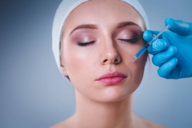 Güzel kadın yüz kozmetik enjeksiyon. Gri arka plan üzerinde izole