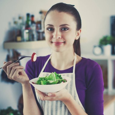 Genç kadın modern mutfakta taze salata yiyor.