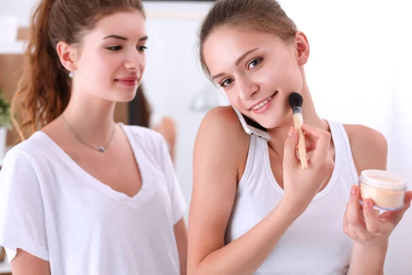 Meninas bonitas olhando no espelho e aplicando cosméticos com uma escova grande — Fotografia de Stock