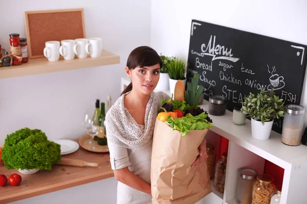 야채 가방을 들고 부엌에 서 있는 젊은 여자 — 스톡 사진