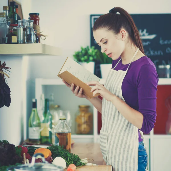 Jonge vrouw die kookboek leest in de keuken, op zoek naar recept — Stockfoto