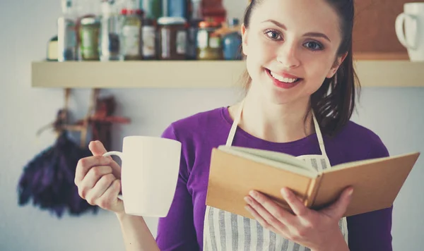 Jovem mulher lendo livro de receitas na cozinha, à procura de receita — Fotografia de Stock