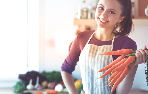 Glückliche junge Frau hält ein Bündel Möhren in der Küche — Stockfoto