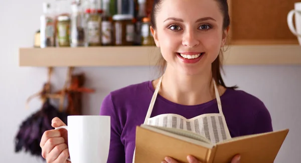 Mutfakta yemek kitabı okuyan genç bir kadın yemek tarifi arıyor. — Stok fotoğraf