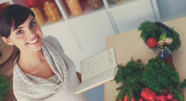 Jovem mulher lendo livro de receitas na cozinha, à procura de receita — Fotografia de Stock