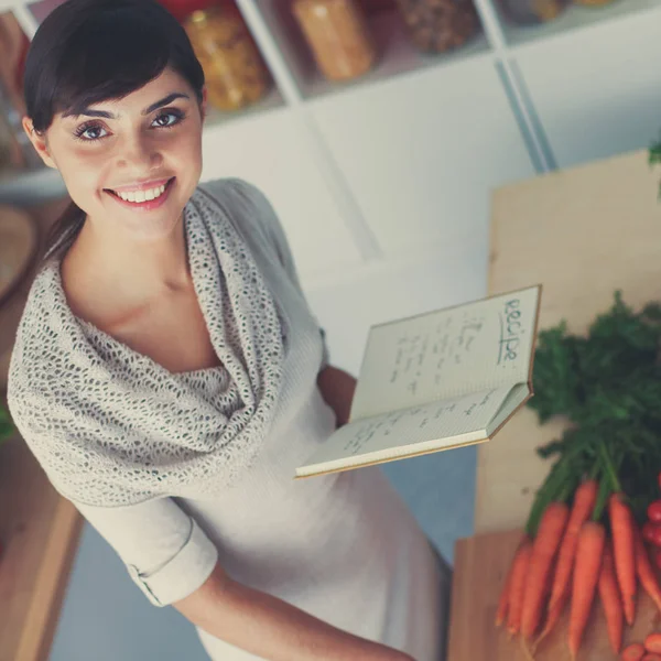 Young woman reading cookbook in the kitchen, looking for recipe — Stock Photo, Image