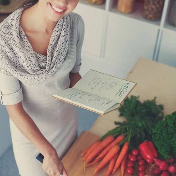 Mujer joven leyendo libro de cocina en la cocina, buscando receta —  Fotos de Stock