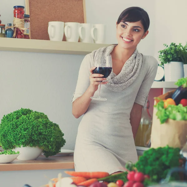 Young woman cutting vegetables in kitchen, holding a glass of wine — Stock Photo, Image