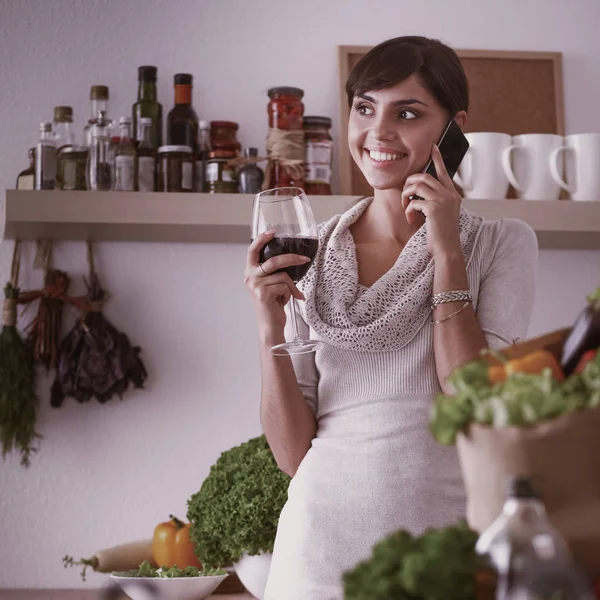 Jovem mulher cortando legumes na cozinha, segurando um copo de vinho — Fotografia de Stock