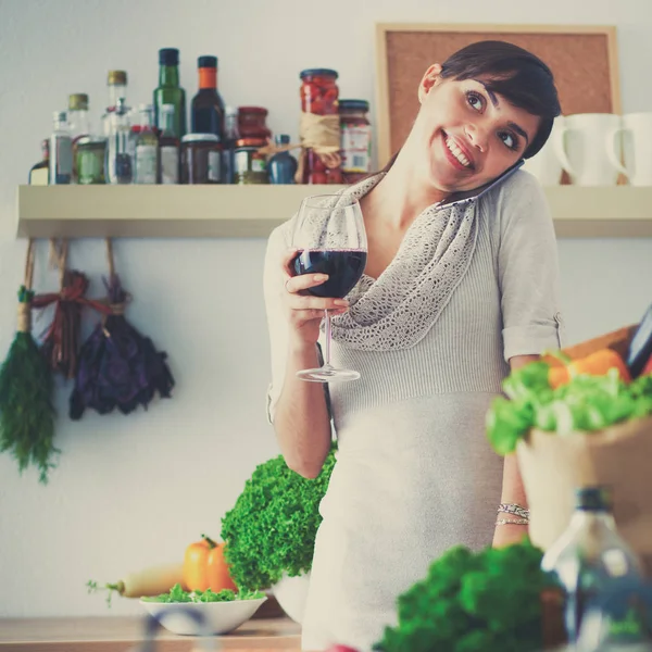 Junge Frau schneidet Gemüse in Küche und hält ein Glas Wein in der Hand — Stockfoto